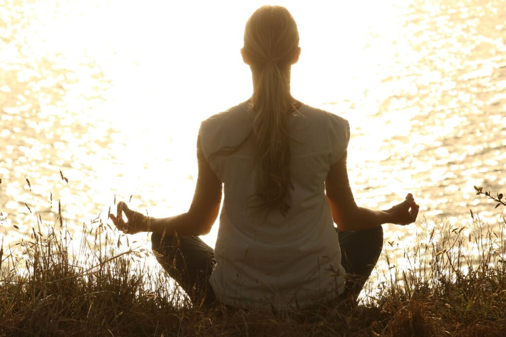 jeune femme en position de méditation dans la nature, devant un lac au soleil couchant