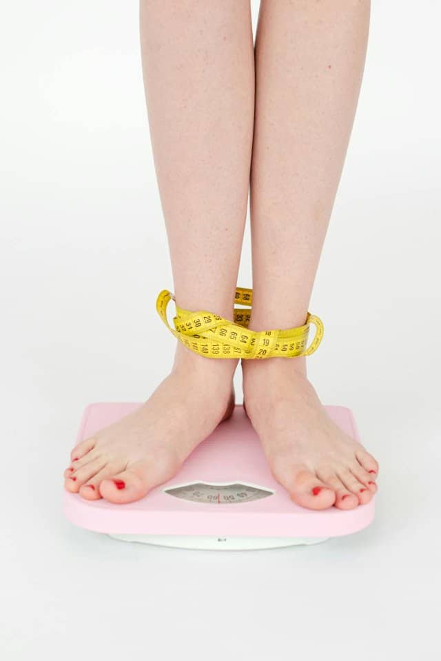 pieds féminins posés sur une balance rose, mètre à couturière enroulé autour des chevilles