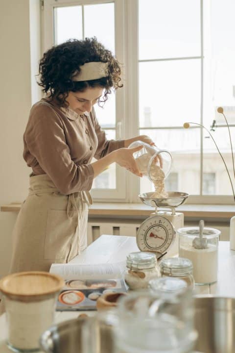 cuisinière qui pèse de la farine sur un outil de balance ancienne dans sa cuisine